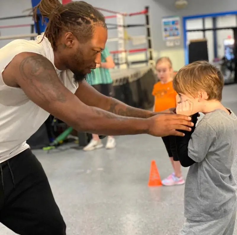 A Dethrone boxing coach helps a young boy keep his hands up.