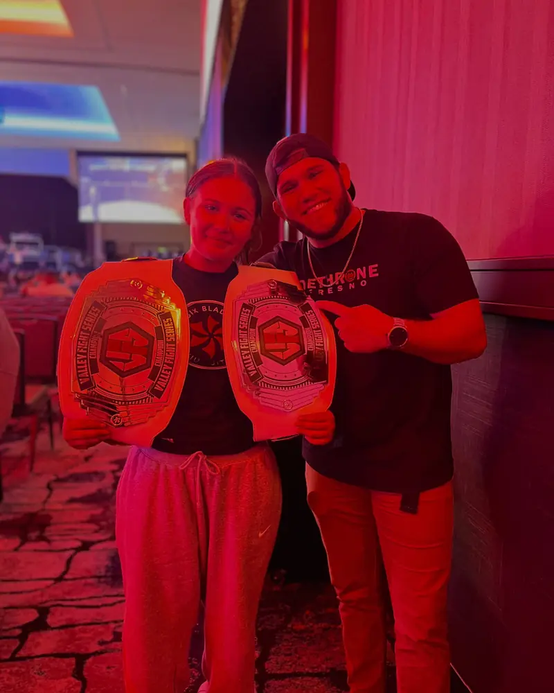 Two Dethrone team members, one in a Dethrone Fresno shirt, hold up championship belts.