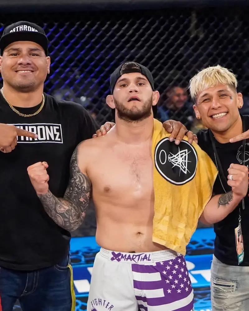 A Dethrone fighter in fight shorts stands in the cage with two Dethrone corner coaches after a fight.