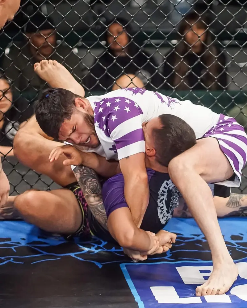 Two fighters grapple against the cage wall during a fight.