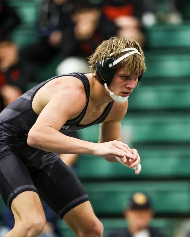Alek VanBebber, in a black singlet and headgear, in his stance during a college match.