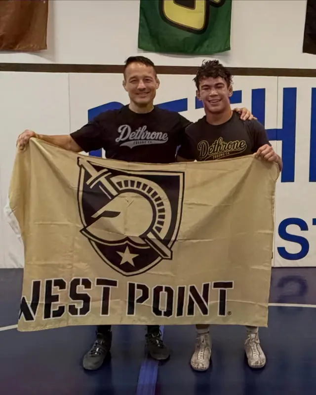 Coach Jason Kraft and Ashton Besmer hold an Army West Point flag on the Dethrone mats.