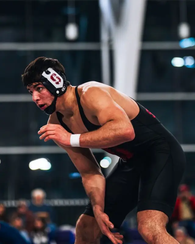 Brokton Borelli in Stanford headgear and singlet, in a wrestling stance during a college match.