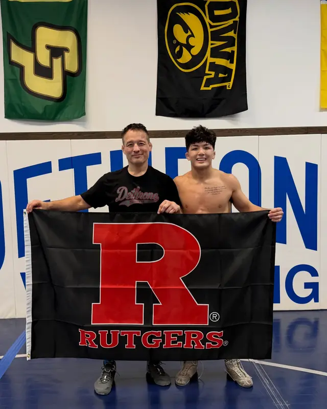 Coach Jason Kraft and CJ Huerta hold a Rutgers flag on the Dethrone mats.