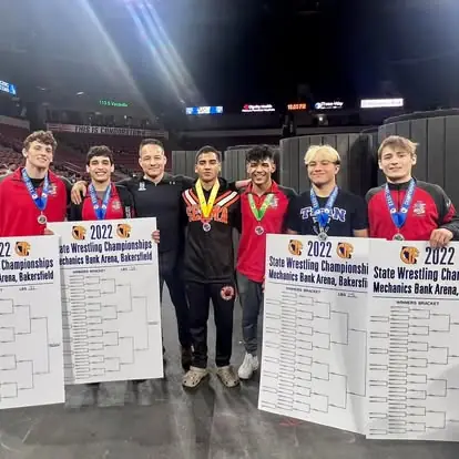 Coach Jason Kraft with six Dethrone wrestlers holding their medals and brackets at the 2022 California state wrestling championships in Bakersfield.