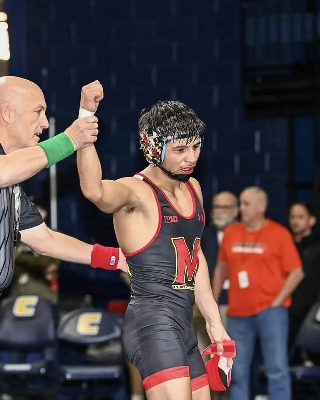 A referee raises the hand of Dario Lemus, in a Maryland singlet.