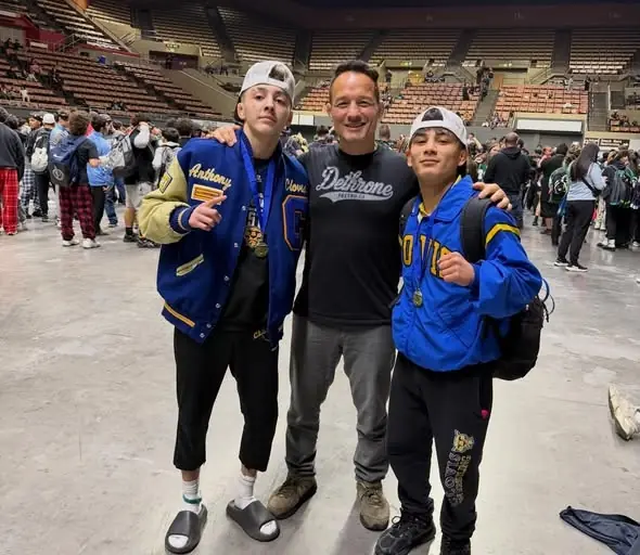 Coach Jason Kraft with two Dethrone wrestlers in their letterman jackets, February 2026.