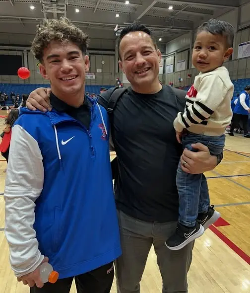 Coach Jason Kraft, holding a toddler, with a Buchanan wrestler at senior night.