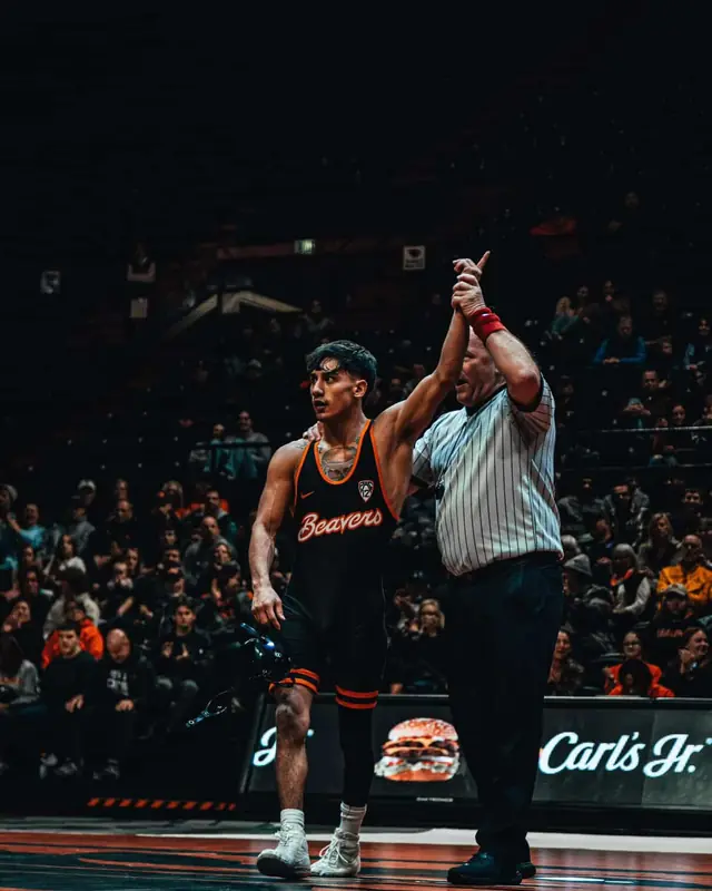 A referee raises the hand of Maximo Renteria, in an Oregon State singlet, after a match in a packed arena.