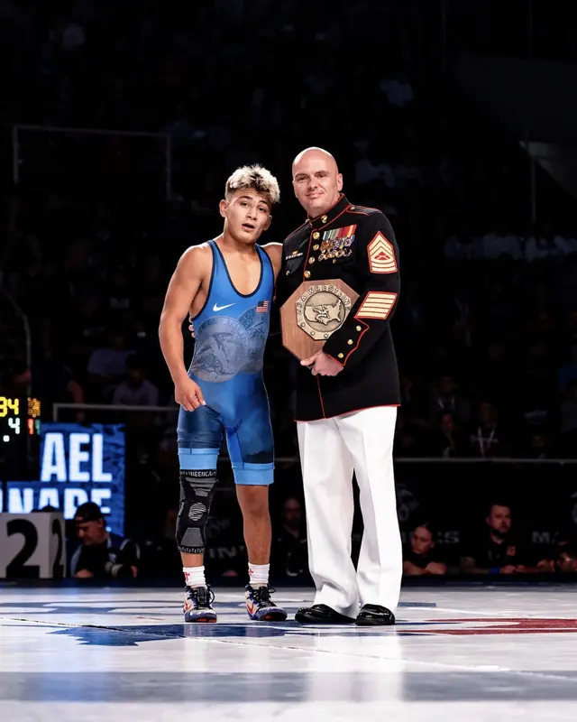 Michael Bernabe, in a blue singlet, stands next to a Marine in dress blues who holds a plaque.
