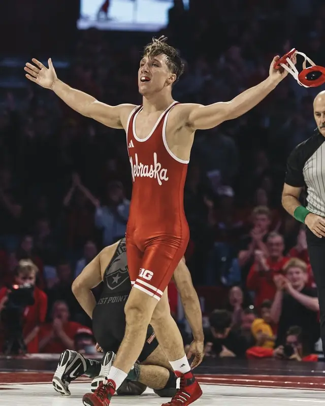 Nikade Zinkin, in a Nebraska singlet, celebrates a win with arms spread wide.