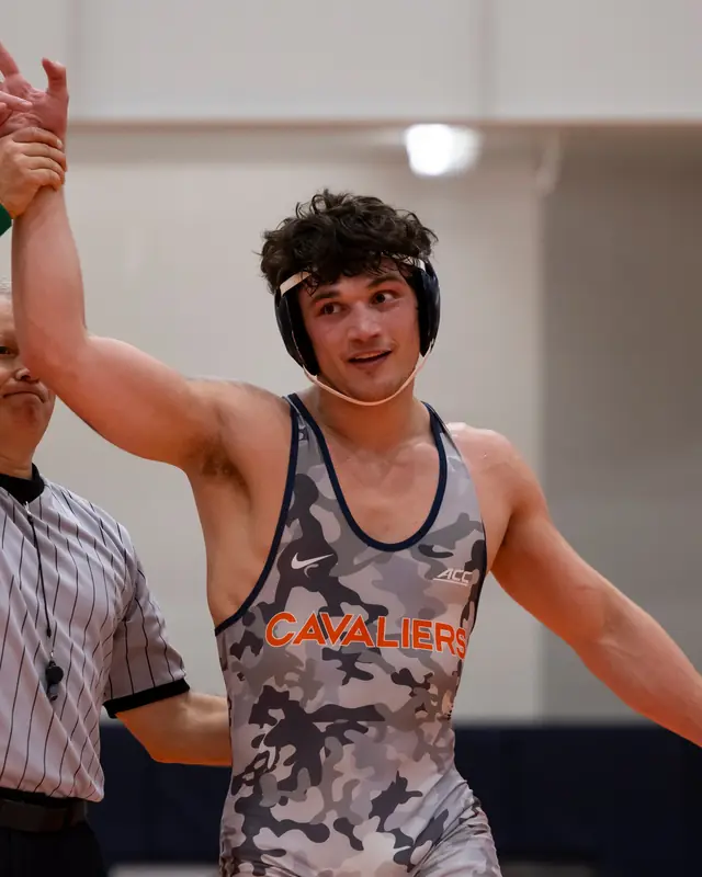 A referee raises the hand of Rocco Contino, in a camouflage Cavaliers singlet, after a college match.