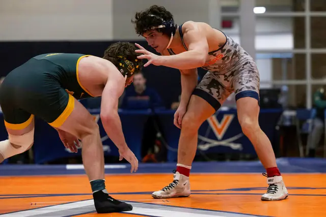 Rocco Contino, in a camouflage singlet, squares up with an opponent in green and gold on an orange mat.
